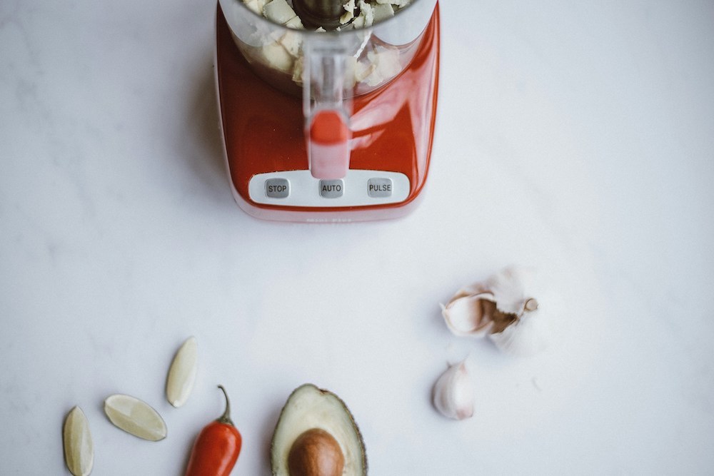 A red color blender with some vegetables near it