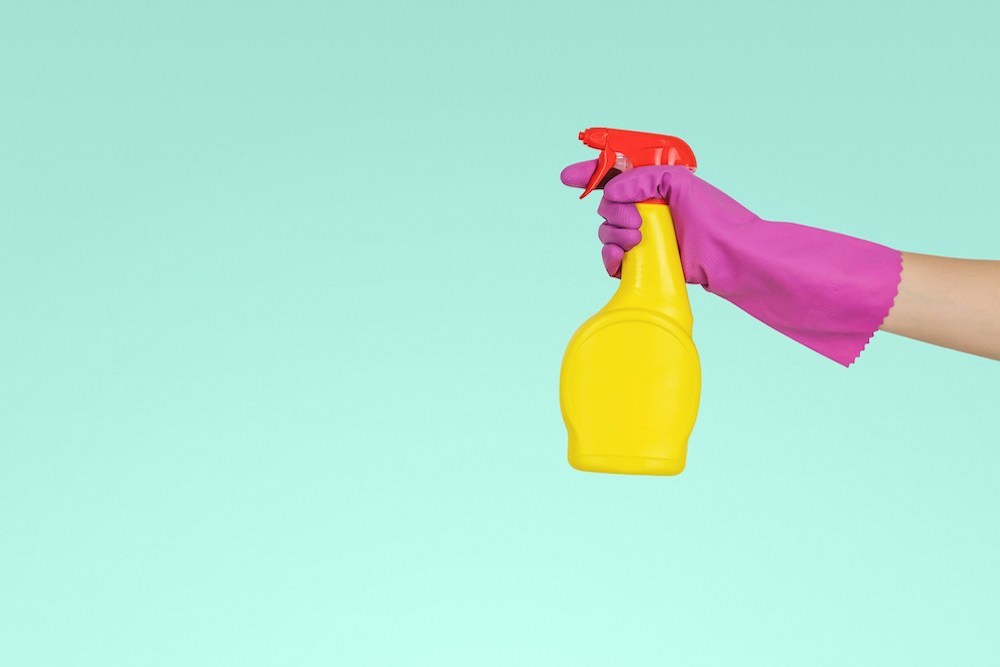 A hand wearing cleaning gloves and holding a spray bottle 